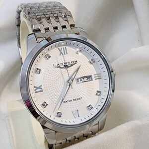 Op de afbeelding: Een zilverkleurig polshorloge met een witte wijzerplaat met Romeinse cijfers, diamantachtige markeringen en de dag van de week. Het horloge heeft een getextureerde wijzerplaat en een roestvrijstalen band. De wijzerplaat leest "LANMSOM" en "WATER RESIST".