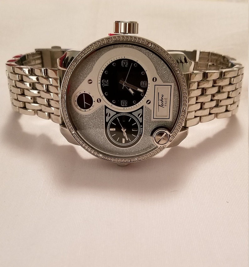 May include: A silver watch with a diamond-encrusted bezel and a multi-layered dial. The watch has a silver metal band and a black face with white accents. The watch face features the text "Techno Pave".
