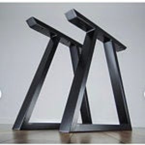 May include: Two black metal table legs in a modern, geometric design. Each leg has a triangular shape with a flat top and angled supports, suitable for a custom table project. The legs are made of sturdy metal.