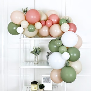 May include: A garland of balloons in shades of green, cream, and blush pink. The balloons are arranged in a cascading pattern and are accented with greenery.