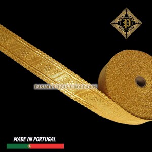 May include: A roll of gold-colored decorative trim with an intricate geometric pattern. The trim is made of a shiny, metallic material and is labeled "PASAMANERIAS Y BORDADOS". The text "MADE IN PORTUGAL" is also visible.