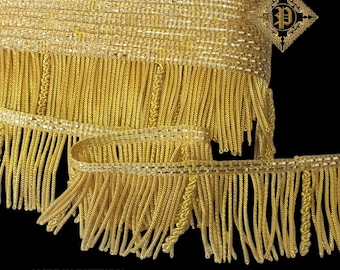 May include: Close-up of a roll of gold fringe trim with a woven top and long, dangling threads. The trim has a metallic sheen and is likely used for embellishments. The text "MADE IN PORTUGAL" is visible at the bottom.