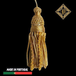May include: A gold tassel with detailed woven patterns and a looped top. The tassel is made of shiny gold threads and has a decorative design. The words "MADE IN PORTUGAL" are at the bottom.