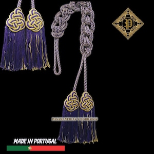 Puede incluir: Conjunto de borlas decorativas moradas y doradas con un cordón trenzado. Las borlas presentan un diseño de nudo. El texto "PASAMANERIAS Y BORDADOS" y "MADE IN PORTUGAL" es visible.