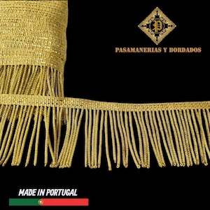 May include: Close-up of gold fringe trim with a woven top edge. The trim is made of shiny, metallic threads and hangs down in long, vertical strands. The text "PASAMANERIAS Y BORDADOS" is displayed above the trim, and "MADE IN PORTUGAL" is at the bottom.