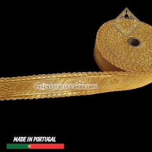 May include: A roll of gold-colored decorative trim with intricate floral and geometric patterns. The trim is labeled "PASAMANERIAS Y BORDADOS" and "MADE IN PORTUGAL". The trim is likely used for embellishing clothing or crafts.