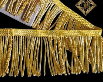 May include: Close-up of gold fringe trim with a woven top and long, dangling strands. The trim features decorative stitching and is set against a black background. The text "MADE IN PORTUGAL" is visible at the bottom.