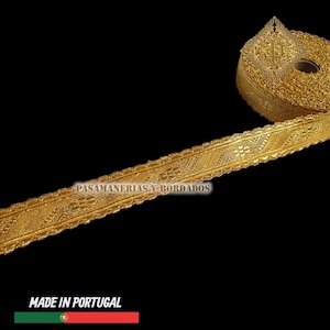 May include: A roll of gold-colored decorative trim with intricate woven patterns. The trim is labeled "PASAMANERIAS Y BORDADOS" and "MADE IN PORTUGAL". The trim has a scalloped edge and is likely used for embellishing clothing or crafts.