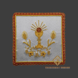May include: A white fabric square with a gold embroidered design of a chalice with wheat stalks and grapes. The fabric has a red and gold border.