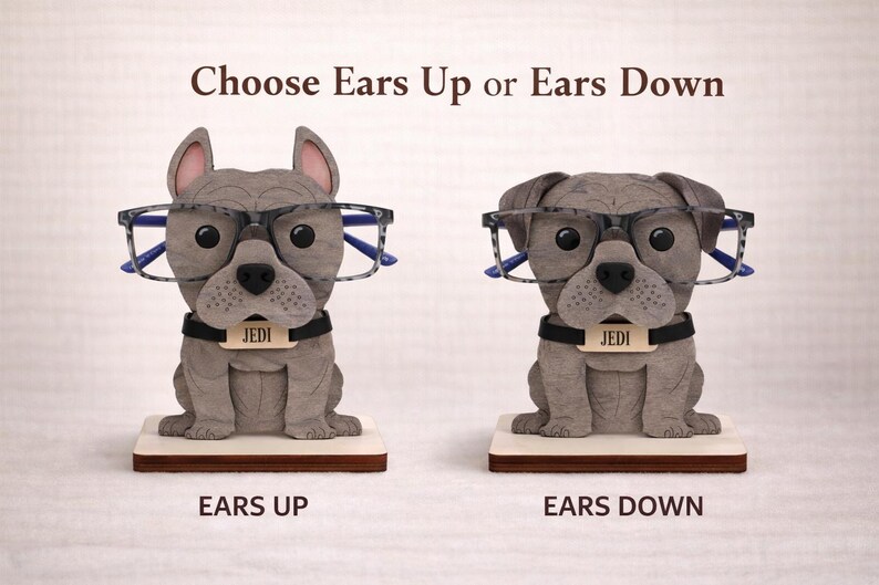 May include: Two gray bulldog-shaped eyeglass holders, one with ears up and the other with ears down, each wearing glasses. The holders have a black collar with the name "JEDI" on a tag. The text "Choose Ears Up or Ears Down" is above the dogs.