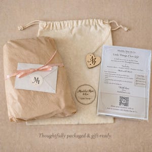 May include: A gift-ready package featuring a wrapped parcel with a pink ribbon, a drawstring bag, and a care kit. The package includes a wooden heart tag with initials and a care kit with instructions. The text "Thoughtfully packaged & gift-ready" is at the bottom.