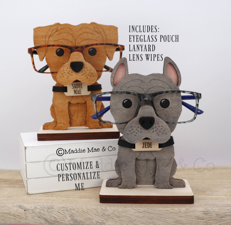 May include: Two wooden dog-shaped eyeglass holders. One is brown with tortoise shell glasses, the other is gray with gray-framed glasses. Each has a name tag. The text "CUSTOMIZE & PERSONALIZE ME" is visible.