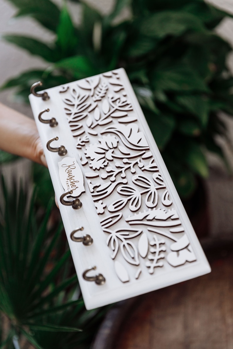 May include: White wooden key holder with a floral design and five hooks. The key holder has a wooden plaque that says "Rauchcher Family".
