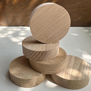 May include: Six unfinished, light-coloured wooden coasters stacked on top of each other. The coasters are circular with visible wood grain. The wood has a natural, unvarnished appearance. Each coaster is approximately 10 cm in diameter.