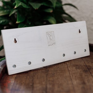 May include: White wooden key holder with five hooks and a logo that says "Should Buy Wood".