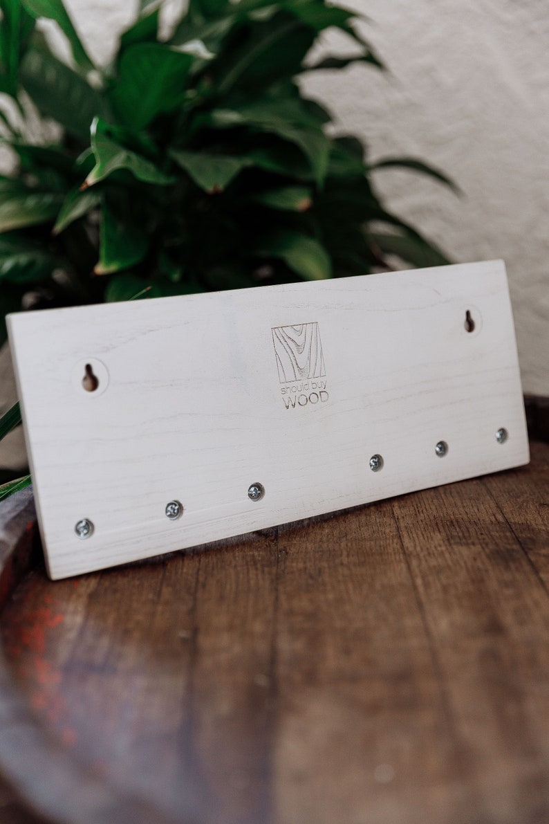 May include: White wooden key holder with five hooks and a logo that says "Should Buy Wood".