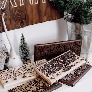May include: Four wooden key racks with intricate laser cut floral designs. Each rack has a personalised nameplate: Hamilton Family, Bride, Sutter, and Smith. The racks are arranged on a white surface.