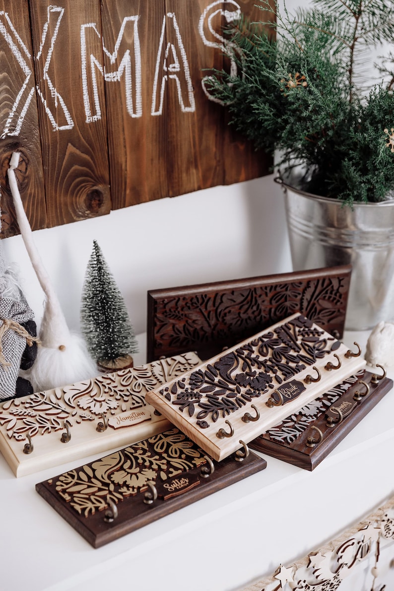 May include: Four wooden key racks with intricate laser cut floral designs. Each rack has a personalised nameplate: Hamilton Family, Bride, Sutter, and Smith. The racks are arranged on a white surface.