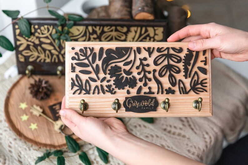 May include: Wooden key holder with a black floral design and the text "Griswold Family". The key holder has three hooks.