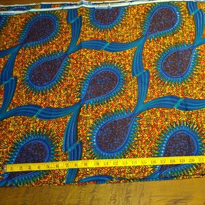 May include: A colorful fabric with a repeating pattern of blue, yellow, orange, and red teardrop shapes with a starburst design. The fabric is measured with a yellow tape measure.
