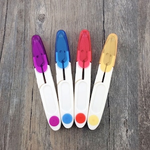 May include: Four pairs of small, white handled scissors with colored plastic tips. The tips are purple, blue, red, and yellow.