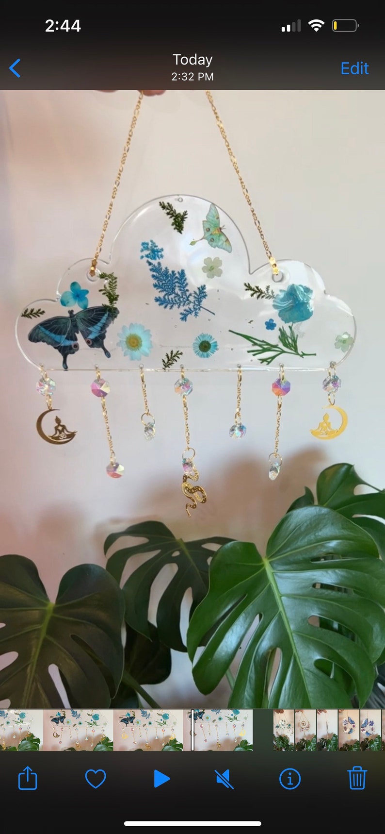 May include: A clear resin cloud-shaped wind chime with pressed flowers and butterflies. The chime has gold chains with crystal beads and charms, including a crescent moon with a meditating figure and a snake.