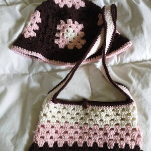 May include: A brown, pink, and white crocheted handbag with a matching crocheted hat. The handbag has a single strap and a brown button closure.