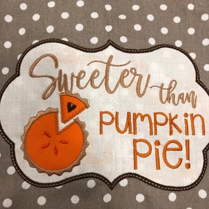 May include: A gray tote bag with white polka dots. The bag features an embroidered design with the words "Sweeter than Pumpkin Pie!" and an orange pumpkin pie slice.