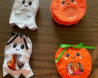 May include: Two sets of Halloween treat bags. One set is white ghost shaped bags with black eyes and a black ribbon. The other set is orange pumpkin shaped bags with black eyes and a green ribbon. Both sets have clear plastic windows to see the candy inside.
