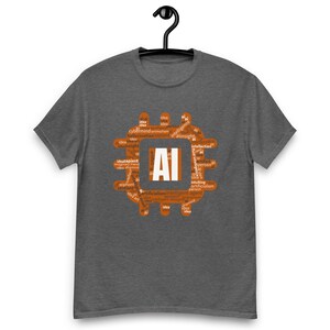 May include: A dark heather gray short-sleeve t-shirt featuring a central orange graphic shaped like a computer chip. The graphic contains the white text AI in the center, surrounded by various small white words related to artificial intelligence.