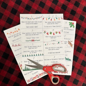 May include: A set of Christmas-themed trivia cards with various holiday-related questions and answers. The cards are white with festive illustrations and text, and are being cut with red scissors. The background is a red and black plaid pattern.