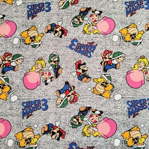 May include: Fabric with a repeating pattern of Super Mario Bros. characters, including Mario, Luigi, Princess Peach, and Bowser. The design includes the text "Super Mario 3" in blue and white speech bubbles on a grey speckled background.