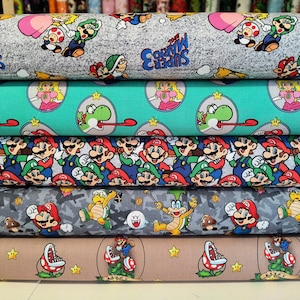 May include: A stack of fabric rolls with Super Mario designs. The fabric features characters like Mario, Luigi, Princess Peach, and Yoshi. The designs are set against various background colours and patterns, perfect for crafting projects.