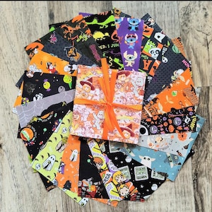May include: A collection of 20 fabric squares featuring Halloween-themed designs. The squares are black, orange, and white with various characters and patterns. The squares are arranged in a fan shape and tied together with an orange ribbon.