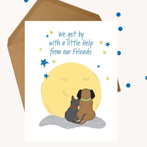 May include: Greeting card with a whimsical illustration of a brown dog and a black cat sitting together, gazing at a yellow moon. The card has the text "We get by with a little help from our Friends" and is accompanied by a brown envelope.