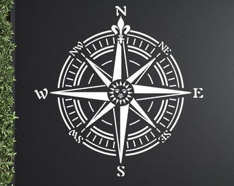 May include: A white wall decal featuring a compass rose design with a central sun face icon. The compass includes cardinal directions N, E, S, W and intercardinal points NE, SE, SW, NW. The graphic is displayed on a dark gray wall surface.