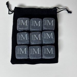 May include: Nine grey stone cubes with the letter "M" and the word "Montes" engraved on each cube. The cubes are in a black velvet drawstring bag.