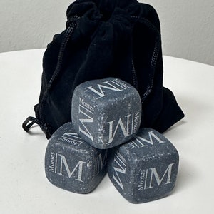 May include: Four grey stone ice cubes with the word "Montes" and the letter "M" engraved on each. The ice cubes are in a black velvet drawstring bag.