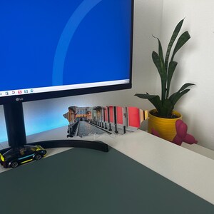 May include: A computer monitor with a blue screen is on a desk with a small toy car, a plant in a yellow pot, and a pink figurine.