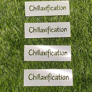 May include: Four white rectangular stencils with the word "Chillaxification" cut out in a handwritten style. The stencils are arranged vertically on a green, artificial grass surface.