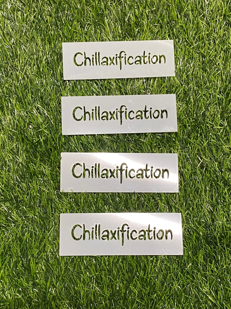 May include: Four white rectangular stencils with the word "Chillaxification" cut out in a handwritten style. The stencils are arranged vertically on a green, artificial grass surface.