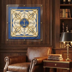 May include: A square silk scarf displayed in a clear acrylic frame, featuring a central blue circle with a gold anchor, surrounded by a cream background with gold rope, blue leather strap motifs, and four silver anchors in the corners.