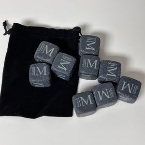 May include: A set of nine grey stone whiskey chilling cubes with the word "Montes" and the letter "M" engraved on each cube. The cubes are in a black velvet pouch.