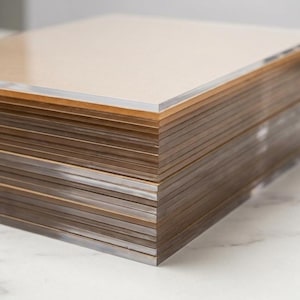 May include: A stack of rectangular, clear acrylic sheets with a light brown hue. The sheets are neatly stacked, showcasing the edges and the transparent quality of the material. The top sheet is a solid light brown color.
