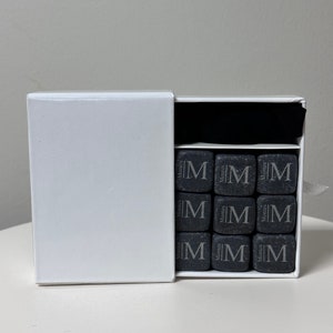 May include: A white box with a black interior containing nine black square whiskey stones with the word "Monties" and the letter "M" engraved on each stone.