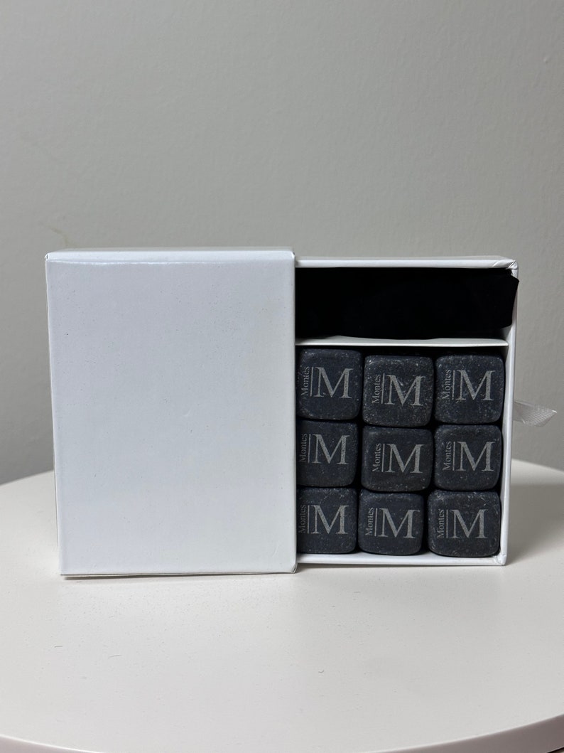 May include: A white box with a black interior containing nine black square whiskey stones with the word "Monties" and the letter "M" engraved on each stone.