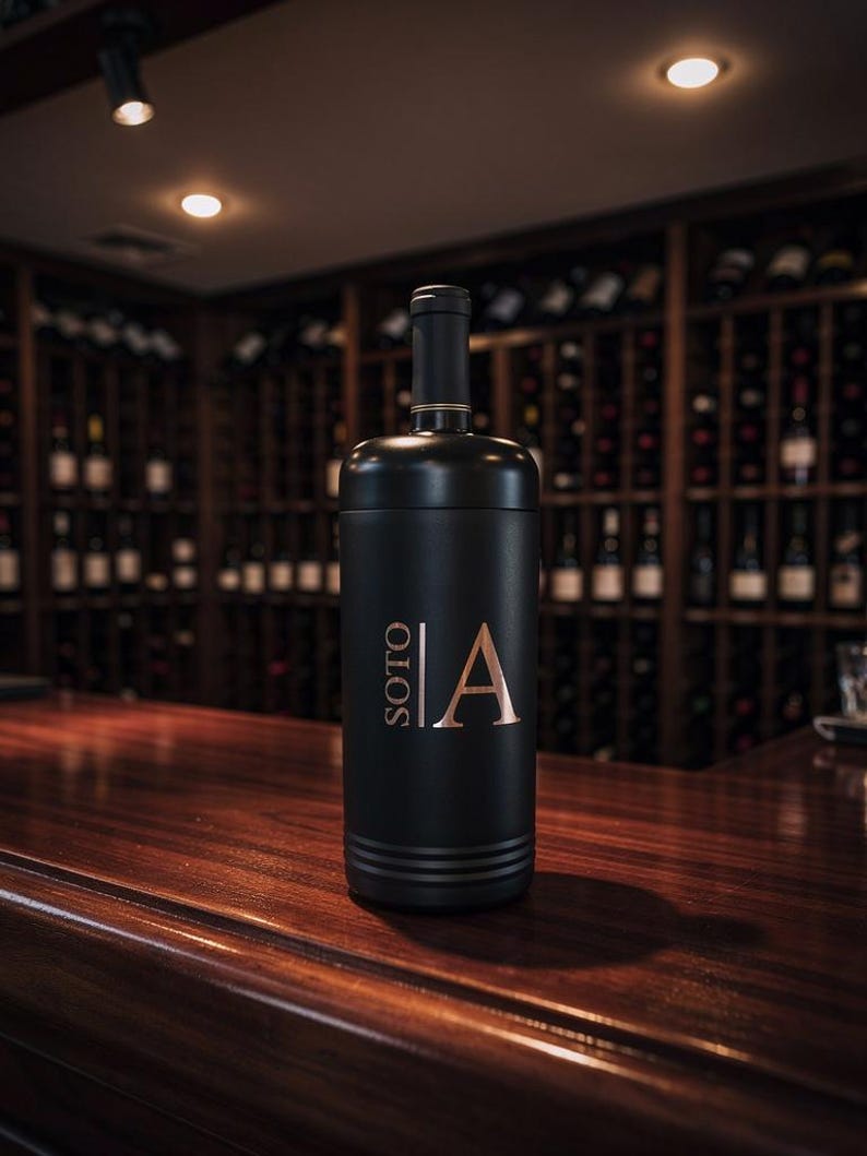 May include: A black wine bottle with gold accents and the word "SOTO" and the letter "A" in gold lettering. The bottle is on a wooden surface, with a wine rack in the background.