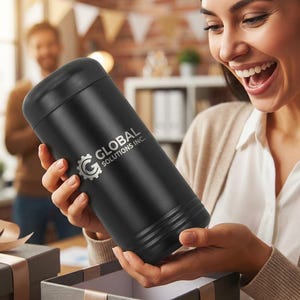 May include: A black cylindrical tumbler with the text "GLOBAL SOLUTIONS INC." in silver. The tumbler is being held by a person opening a gift box. The background shows other people and a desk.
