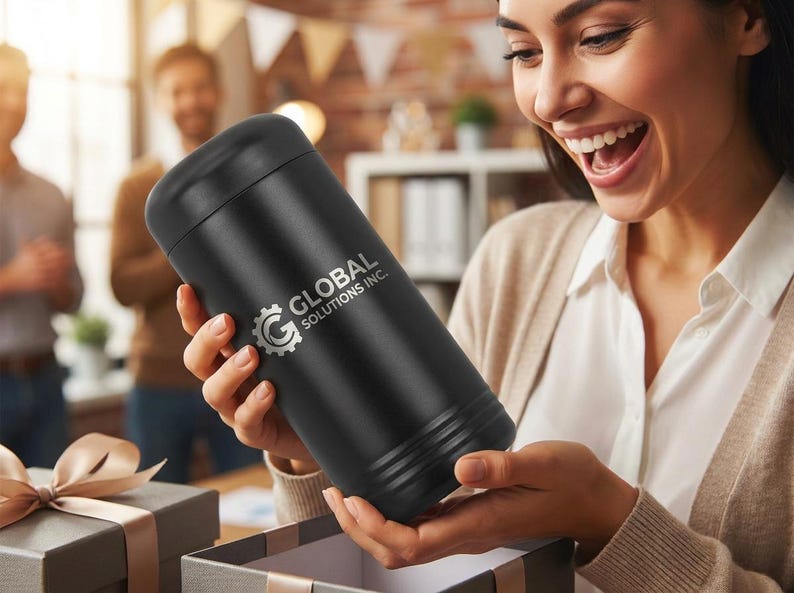 May include: A black cylindrical tumbler with the text "GLOBAL SOLUTIONS INC." in silver. The tumbler is being held by a person opening a gift box. The background shows other people and a desk.