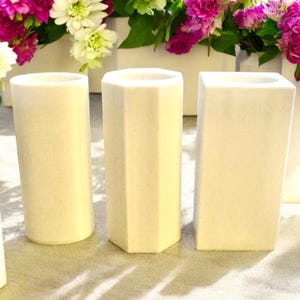 May include: Three white ceramic candle holders, one round, one hexagonal, and one rectangular.